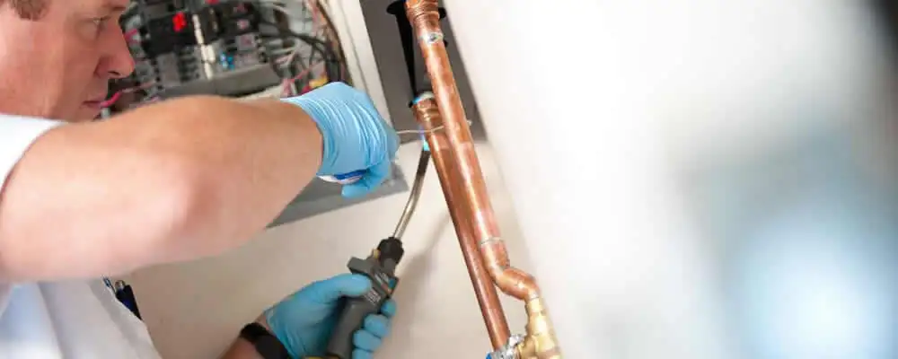 Water heater repair technician testing copper pipe connections and controls in Baltimore, MD